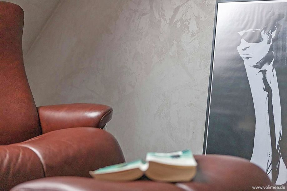 Ein gemütlicher Wohnraumausschnitt, welcher eine individuelle Wandgestaltung in grau im Hintergrund zeigt.